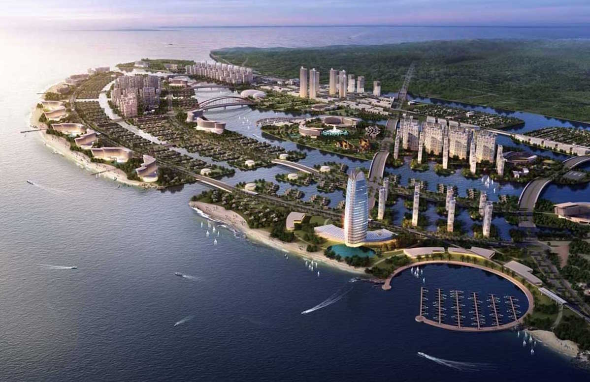 Hình ảnh từ trên cao của dự án Vinhomes Cần Giờ, bao gồm bến du thuyền hình tròn, các tòa nhà cao tầng, khu vực xanh với công viên ven biển, và bãi biển trải dài. Các cây cầu nối liền các khu vực, kết hợp hài hòa giữa kiến trúc và thiên nhiên.